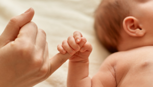 Fotografía para artículo de blog topfarma sobre la vitamina D en bebés. En la fotografía vemos a un bebe tumbado agarrándose con una mano al dedo de su madre.
